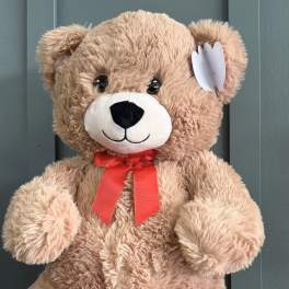 Large tan teddy bear with a red ribbon bow