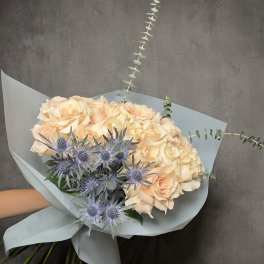 Bouquet of pale peach roses with blue thistle in light wrapping