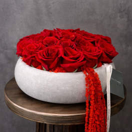 Round box filled with red roses and a trailing red beaded ribbon
