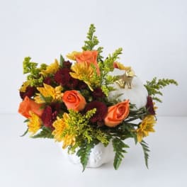 Orange roses and yellow mums in a white pumpkin vase