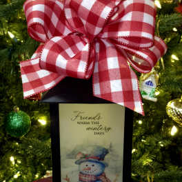 Gift box with a red plaid bow and a snowman card in front of a Christmas tree