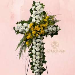 Cross-shaped floral tribute with white and yellow flowers on a stand
