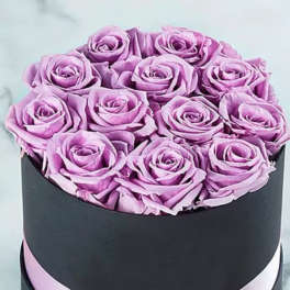 Lavender roses arranged in a black round box with a pink ribbon