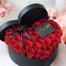 Heart-shaped box filled with red roses and tied with a black ribbon