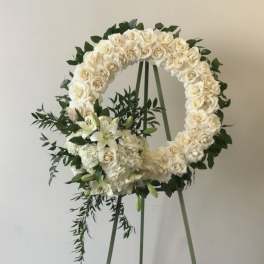 White rose wreath on an easel with lilies and greenery