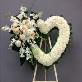 Heart-shaped white floral wreath on an easel with a small bouquet of pale roses