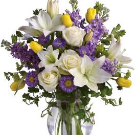 Bouquet of white lilies, roses, purple flowers, and yellow tulips in a glass vase