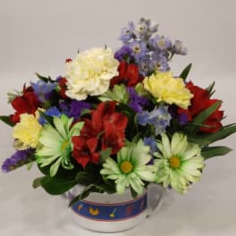 Mixed bouquet of red, yellow, white, and blue flowers in a ceramic mug
