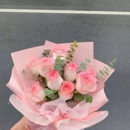 Handheld bouquet of pink roses wrapped in pale pink paper
