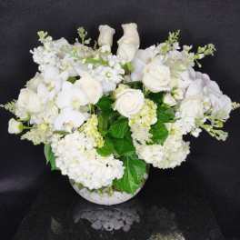 White roses and orchids arranged in a round glass vase