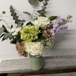 Mixed bouquet of roses, hydrangea, and lavender flowers in a pale green vase