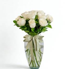 White roses in a clear glass vase with a ribbon bow