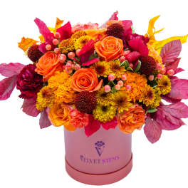 Orange and yellow mixed bouquet in a pink hatbox with magenta foliage