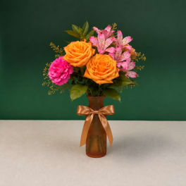 Orange roses and pink alstroemeria in an amber vase with a ribbon