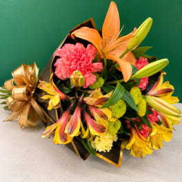 Bouquet of orange lilies, pink carnations, and yellow alstroemeria wrapped in black paper with gold ribbon