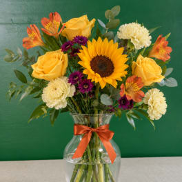 Bouquet of yellow roses, a sunflower, carnations, and alstroemeria in a glass vase