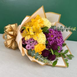 Bouquet of yellow, purple, and white flowers wrapped in gold-trimmed paper