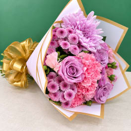 Pink and lavender bouquet wrapped in white paper with a gold ribbon