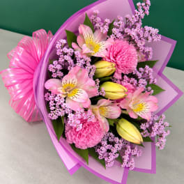 Pink bouquet with lilies, carnations, and purple filler flowers wrapped in purple paper