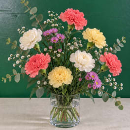 Mixed carnations and purple daisies in a clear glass vase