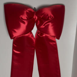 Large red satin bow with long ribbon tails hanging on a wall