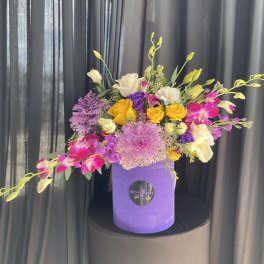 Colorful bouquet in a purple hatbox with yellow, pink, white, and purple flowers