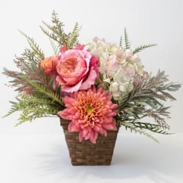 Pink and peach flowers in a woven basket with airy greenery