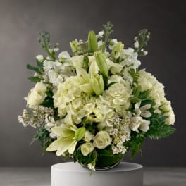 White floral arrangement with lilies, roses, and hydrangeas in a low vase