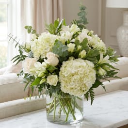 White flowers arranged in a clear glass vase with green foliage