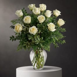 White roses arranged in a clear glass vase with mixed greenery