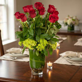Red roses in a glass vase with green flowers on a dining table