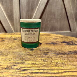 Green glass candle jar with a beige label on a wooden surface