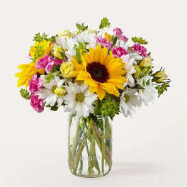 Bouquet of sunflowers, daisies, and pink carnations in a glass mason jar