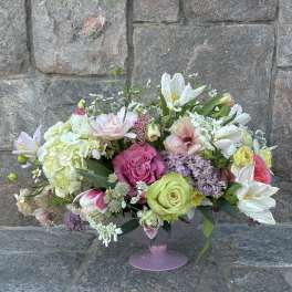 Low pink compote filled with pink roses, white tulips, hydrangeas, and mixed pastel blooms.
