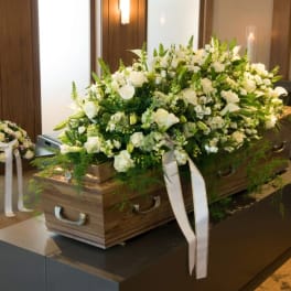 White floral casket spray with ribbons on a wooden coffin
