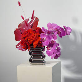 Red roses and purple orchids arranged in a silver vase