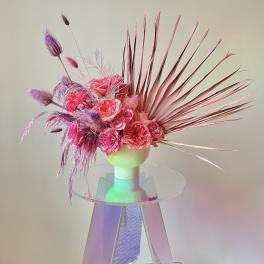 Pink and purple floral arrangement in a white vase with fan-like palm fronds