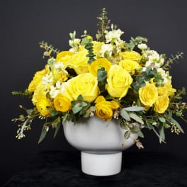 Yellow roses and ranunculus in a white pedestal vase