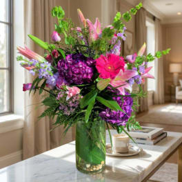 Colorful bouquet of lilies, gerbera daisies, and purple flowers in a glass vase