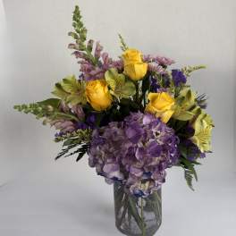 Bouquet of yellow roses, purple hydrangea, and mixed blooms in a glass vase