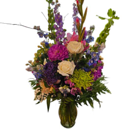 Tall mixed flower arrangement in a glass vase with purple, pink, and cream blooms