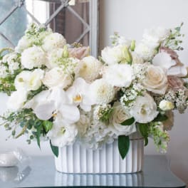 White floral arrangement in a ribbed white vase with pale pink accents