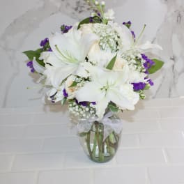 White lilies and roses in a glass vase with purple filler flowers