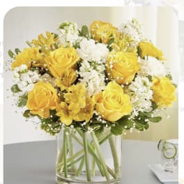 Yellow roses and white flowers arranged in a clear glass vase