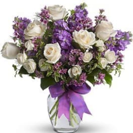 White roses and purple flowers arranged in a glass vase with a purple ribbon