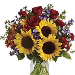 Bouquet of sunflowers, red roses, and purple daisies in a glass vase