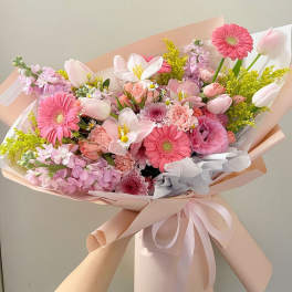 Pink mixed bouquet with gerbera daisies, tulips, and lilies wrapped in pastel paper
