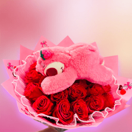 Pink teddy bear resting on a bouquet of red roses