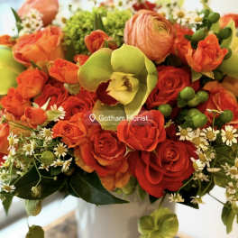 Bouquet of red and orange roses with green orchids in a white vase