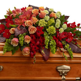 Floral casket spray with red, peach, and green blooms on a wooden casket